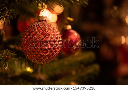 red christmas decoration on a christmastree with lights in the background