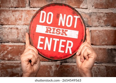 Red Circular Warning Sign with Text “Do Not Risk Enter” Held Against Brick Wall.
