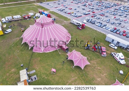 Red circus tent seen from aerial perspective standing on a grass field next to car parking lot. Entertainment concept. High quality photo