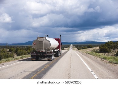 Red classic big rig semi truck with tank trailer for liquid fuel and lubricants makes overtaking in the opposite lane of traffic on a straight road in the desert of Nevada