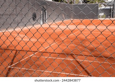 Red clay tennis court surface seen through chain link metal fence - Powered by Shutterstock