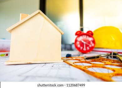 Red clock on archetecture blueprint with pencil, yellow helmet, wooden house model and engineering equipments in modern working office room  - Powered by Shutterstock