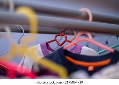 Red Clothes Hanger In The Shape Of A Heart In The Middle Of The Clothesline. Form Of Love Between Colorful Objects.