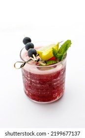 Red Cocktail, Rasberry Mojito, A Long Drink In A Glass, With Ice Cubes, Rasberries, Garnished With American Blueberries, Mint Leaves And Lemon, Isolated On White Background, Selective Focus.