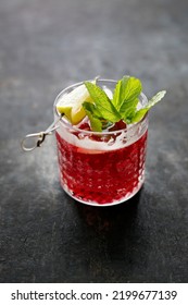 Red Cocktail, Rasberry Mojito, A Long Drink In A Glass, With Ice Cubes, Rasberries, Garnished With Mint Leaves And Lemon, On Black Stone Background, Selective Focus.
