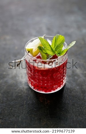 Red cocktail, rasberry mojito, a long drink in a glass, with ice cubes, rasberries, garnished with mint leaves and lemon, on black stone background, selective focus.