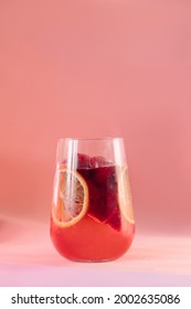 red cocktail with soda in a large glass glass on a pink background