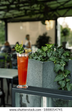 The red cocktail in the summer restaurant terrace. Red tall cocktail decorated with ice and mint