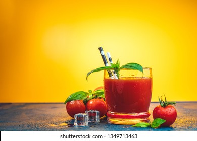 Red cocktail with tomato juice between tomatoes, fresh basil and ice. Delicious tomato bloody mary cocktail on dark blue concrete table with spot light. Yellow background.