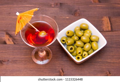 Red Cocktail With Umbrella And Olives On A Wooden Table Seen From Above