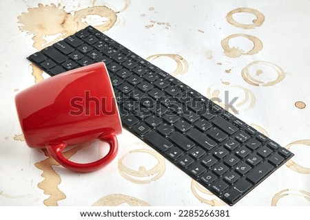 Red coffee cup overturned on a computer keyboard on a table with coffee stains. Keyboard filled with coffee drink