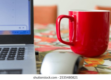 A red coffee mug sits on a table next to a laptop. The laptop is open and the screen is displaying a graph. Concept of productivity and focus - Powered by Shutterstock