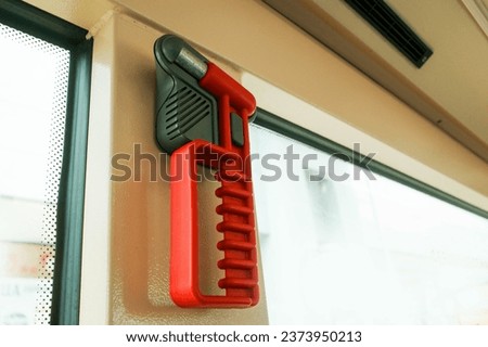 A red color glass window breaker near a breakable window inside a bus. It is used to smash the window in emergency situation.