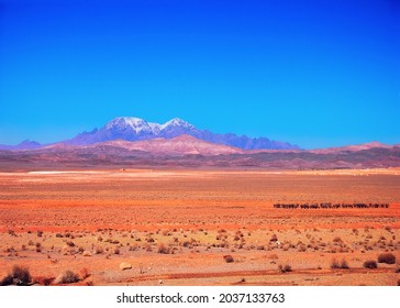 Red colorful desert against the background of purple and violet mountains covered with snow and blue sky. Amazing nature scenery near Tehran - Isfahan road, Iran, Middle East, Western Asia.