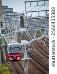 Red commuter train reflects the overhead aluminium strutures and electrically wires off the driver