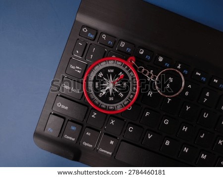 A red compass keychain is placed directly on top of the character keys of a black computer keyboard.