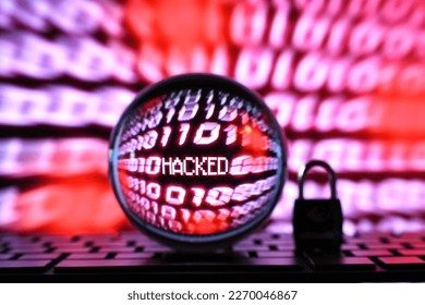 Red computer code binary number stream screen with word hacked seen through lens ball with lock padlock on keyboard. Concept for hacker cyber attack, fraud, scam