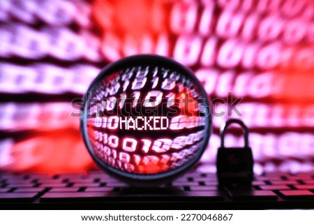 Red computer code binary number stream screen with word hacked seen through lens ball with lock padlock on keyboard. Concept for hacker cyber attack, fraud, scam