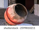 Red concrete mixer with wet cement inside at construction site. Close-up shot of rotating drum covered in dried cement. Industrial construction and building process concept.