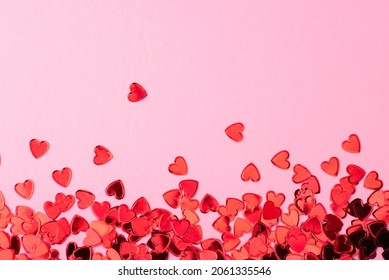 Red confetti in the form of hearts on a pink background. Valentines day backdrop. Flat lay style with minimalistic design. Template for banner or party invitation