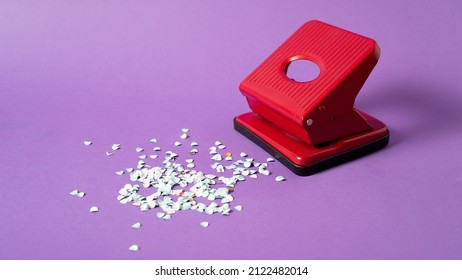 Red confetti maker. Hole puncher machine. Paper punch sprinkle. Hole punch art. Red puncher on violet background