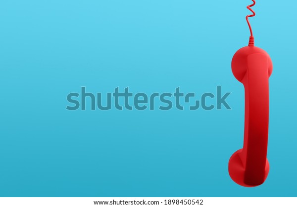Red corded telephone handset\
hanging on light blue background, space for text. Hotline\
concept
