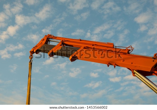 Red crane boom\
against the blue sky. Car manipulator unloads the pipe.\
Construction works. Summer. Sunny\
day.