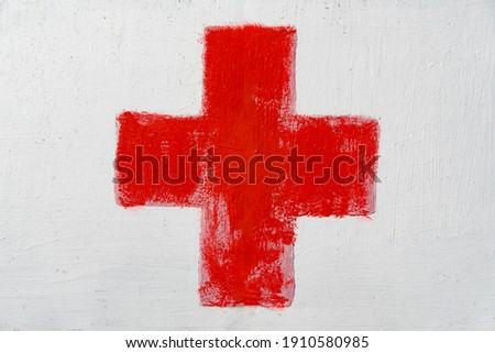 Red cross painted by hand on white wall. First aid kit medical icon. Medicine health hospital sign or emergency medicine symbol, health care.