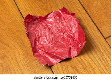 Red Crumpled Candy Wrapper On A Wooden Floor