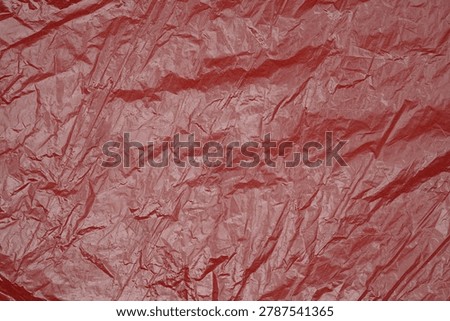 Red crumpled nylon texture background. Wrinkled plastic surface with glossy folds and abstract pattern. Modern creative backdrop with vibrant monochrome color and detailed synthetic texture                              