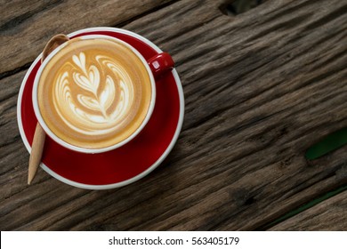 Red cup of cappuccino with beautiful latte art on old wooden background. Top View.