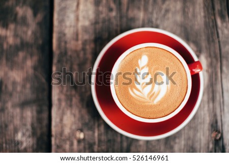 Red cup of cappucino with beautiful latte art on old wooden background. Top View.