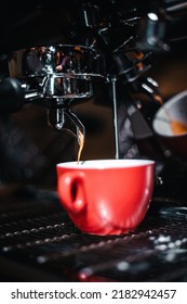 Red cup of coffee at the coffee maker machine, coffee time. Blurred background. High quality vertical photo