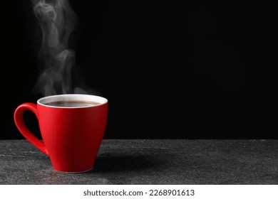 Red cup with hot steaming coffee on grey table against black background, space for text - Powered by Shutterstock