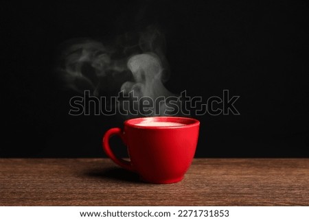 Red cup with hot steaming coffee on wooden table against black background