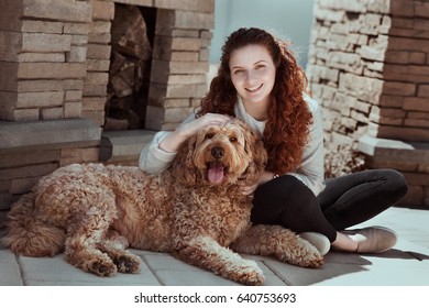 Red Curly Hair Dog And Girl Hugging Sitting Next To Fire Place