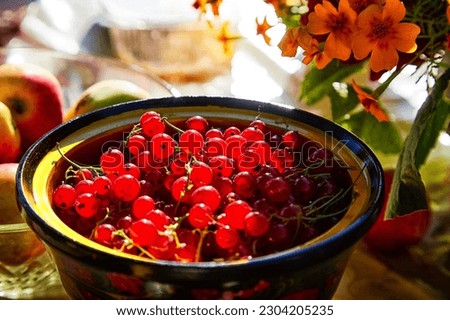 Red currant berries in a wooden plate on the table and a blurred background with red flowers