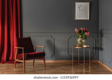 Red Curtain And Burgundy Armchair Standing In Grey Room Interior With Pink Tulips On Gold End Table And Simple Poster Hanging On The Wall With Wainscoting