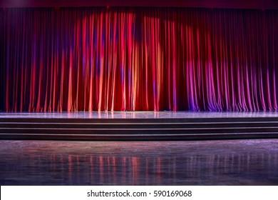 Red Curtains And The Stage Parquet With Stairs In Theater With Colorful Lighting.