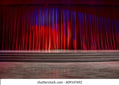 Red Curtains And The Stage Parquet With Stairs In Theater With Colorful Lighting.