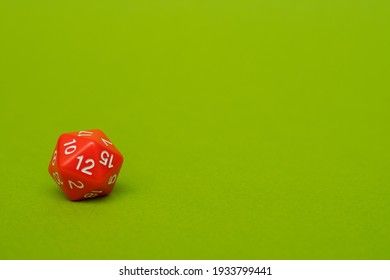 Red D20 dice on a green background: space for text, side view, concept of role-playing games and games for the whole family at home