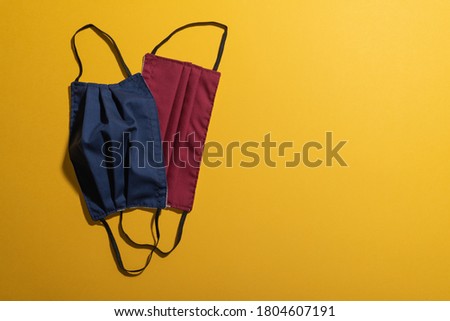 Red and dark blue facemasks flat lay on mustard yellow plain background. Poster template with copy space