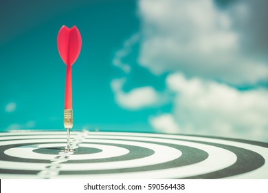 Red dart arrow hitting in the target center of dartboard with blue sky background - Shutterstock ID 590564438