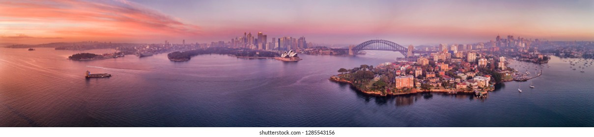 Red Dawn Sun Light Reflecting In Waters Of Sydney Harbour And Bays Around Waterfront Of Sydney City CBD With Landmarks In Wide Aerial Panorama.