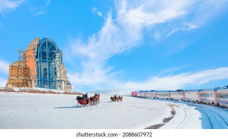Red diesel train (East express) in motion at the snow covered railway - Horses pulling sleigh in winter - Ani Ruins, Ani is a ruined and  medieval Armenian city - Kars, Turkey