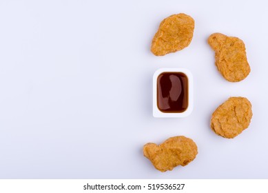 Red dip sauce in plastic container surrounded by four chicken nuggets which form a half circle, isolated on white background