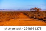 red dirt road through the middle of the desert in karijini national park, western australia; australian outback with red rocks and mountains in the background	