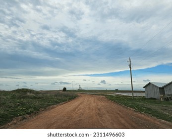 A red dirt road under a cloudy afternoon sky with a lighthouse in the far distance. - Shutterstock ID 2311496603
