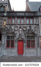 The red door of the stunning Basilica of the Holy Blood in Bruges, Belgium. Gothic facade with golden statues and beautiful stone ornaments. West Flanders, Europe