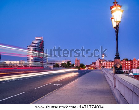 Red double decker bus trails on Putney bridge agains blue sky in London
